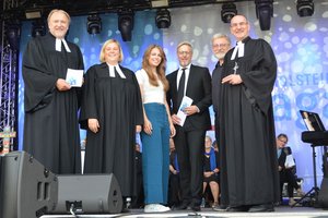 Sechs Menschen stehen auf einer Bühne und lächeln in die Kamera