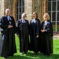Ein Mann und drei Frauen in geistlicher Kleidung stehen im Sonnenschein auf einer Wiese, im Hintergrund eine Kirche.